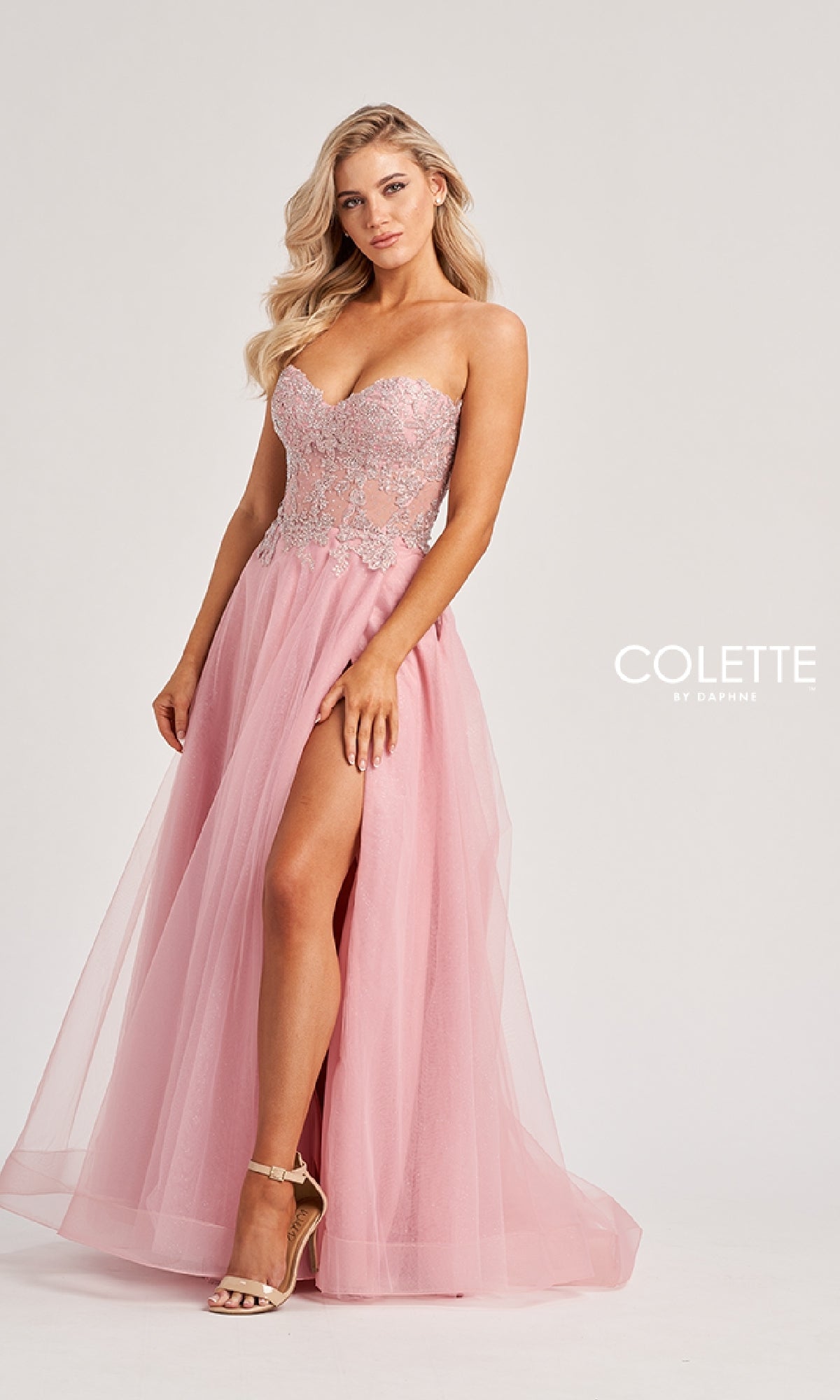 A woman models the Colette CL8110 long prom dress, featuring a strapless pink gown with an embroidered corset bodice, high slit, and elegant A-line skirt against a plain light background.